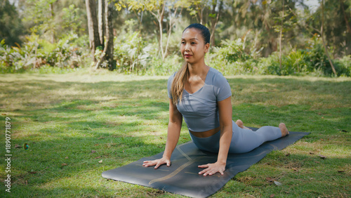 Yoga asian woman outdoor stretching on mat in park sunlight serene expression practicing cobra pose