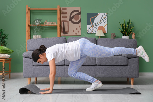 Beautiful pregnant woman with yoga mat in living room