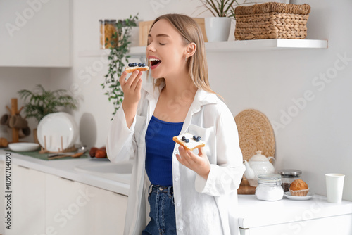 Beautiful young happy woman holding tasty toasts with fresh butter and bluebe...