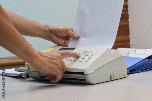 Man hands using a fax machine, putting paper in and sending fax in office