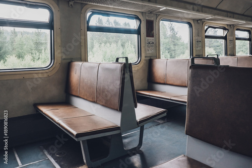 two rows empty benches sit in train car. windows show green landscape outside. scene captures moment during journey. close up.