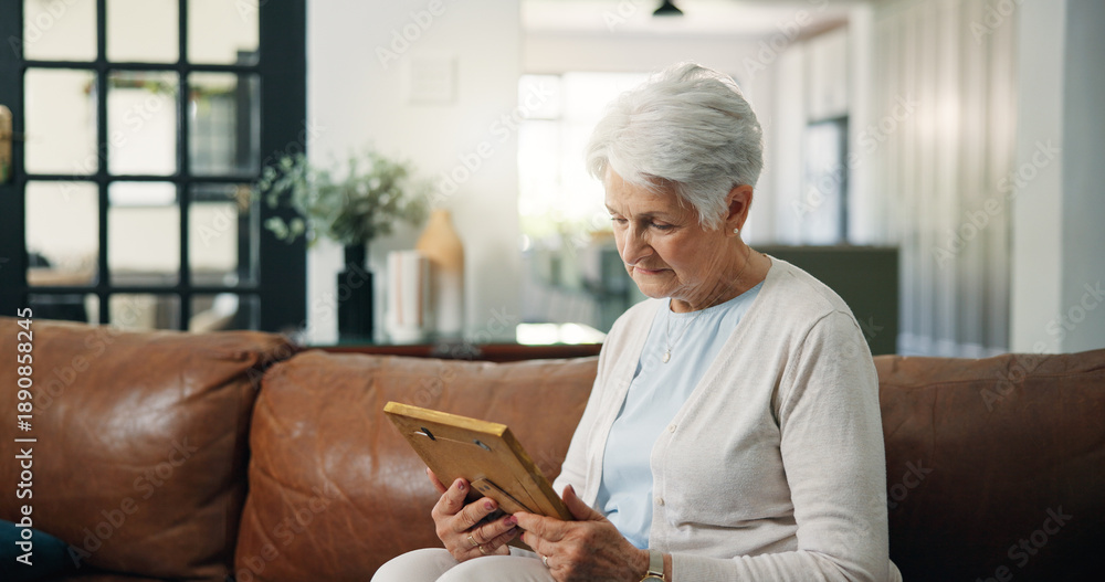 Fototapeta premium Senior woman, photo frame and sad on sofa with memory, grief and nostalgia in lounge at house. Elderly patient, picture and remember with depression, mental health and broken hearth in living room