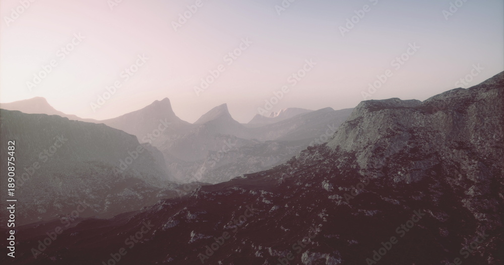 Naklejka premium The landscape features rugged mountains bathed in soft morning light, creating a serene atmosphere. The peaks rise majestically, capturing the beauty of natures tranquility.