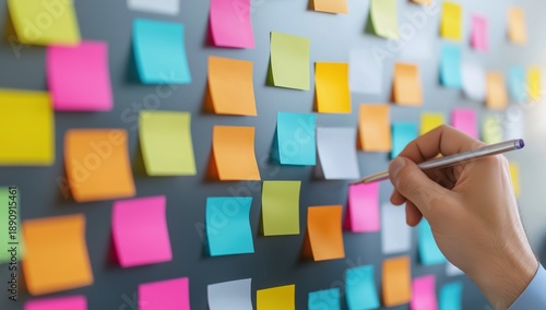 Hand writing on colorful sticky notes on gray wall for planning and brainstorming in office or creative workspace environment