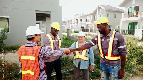 Four construction workers in hard hats hands clasped together in the center at a building site, exchanging ideas and fostering teamwork while discussing their project.