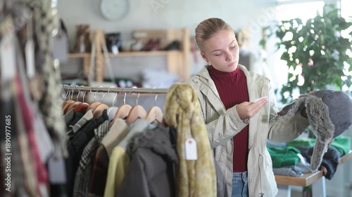 Attentive teen girl customer holding warm fur hat during winter sale in retail outlet 