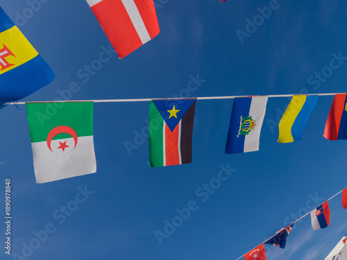 International flags from various nations hang on bunting lines against clear vibrant blue sky. Perfect for global themes multicultural events and world unity celebrations