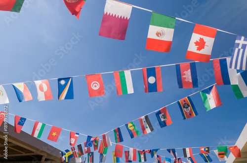 International flags from various nations hang on bunting lines against clear vibrant blue sky. Perfect for global themes multicultural events and world unity celebrations