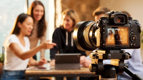 A camera on a tripod in front of a group of people sitting at a table
