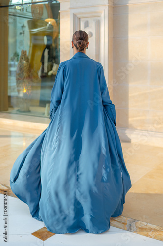 Qatar, Doha, 17.10.2022: Rear view of a woman in a long blue abaya standing in an elegant architectural interior.