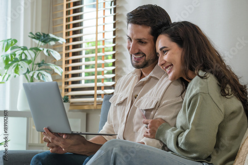 Couple online shopping uses a credit card to buy a product on a laptop, smiling during a purchase at home through a payment app, e-business transaction in cyberspace with a shopping cart,