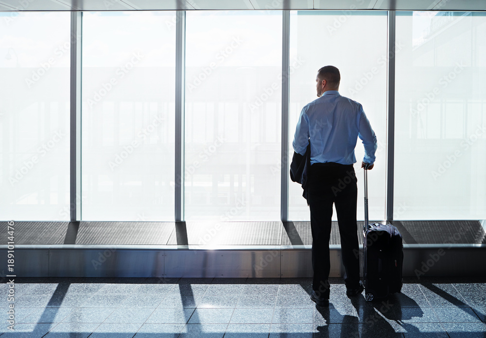 Fototapeta premium Thinking, travel and businessman at airport with luggage, international journey or idea by window. Vision, suitcase and person waiting for flight, trip or immigration with back of professional