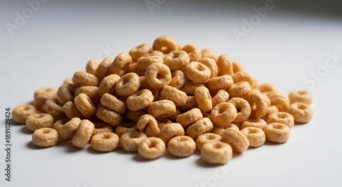 A pile of small, light-tan, ring-shaped cereal pieces sits on a white surface