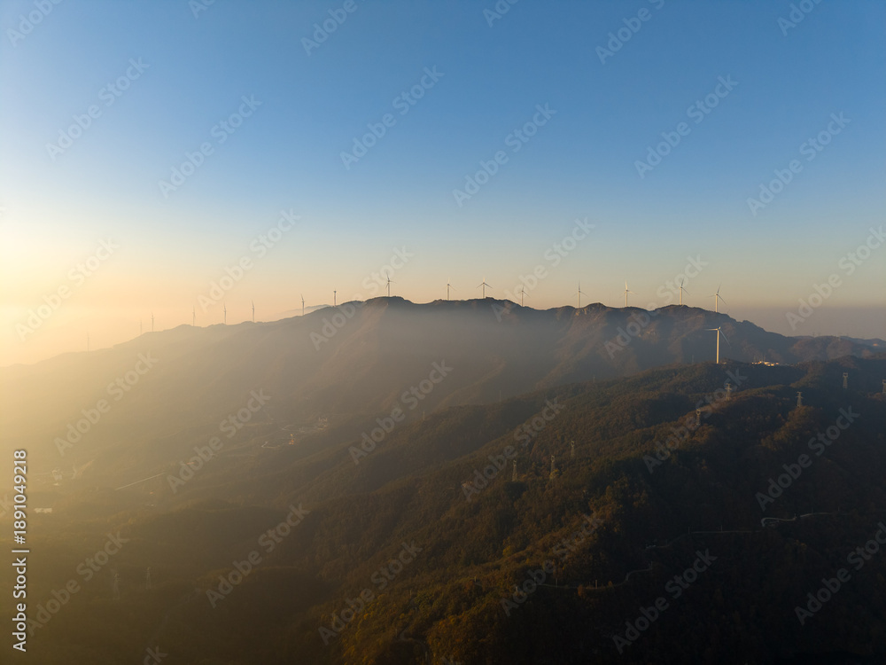 Fototapeta premium Wind turbines on a misty mountain range in Wuhan, China during sunrise
