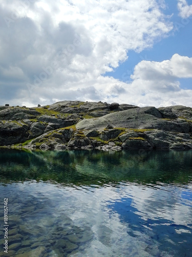 Calm Alpine Pond Reflecting Blue and Gray Summer Clouds on a High Mountain Plateau in Trentino Alto Adige, Italian Alps