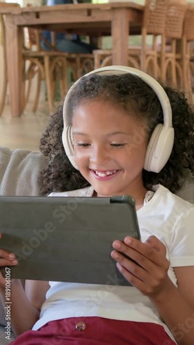 Vertical video: Watching child in white headset and red pants reacting to tablet at home for fun