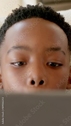 Vertical video: Watching child tracking motion as lowering tablet on beige couch, green-striped tee