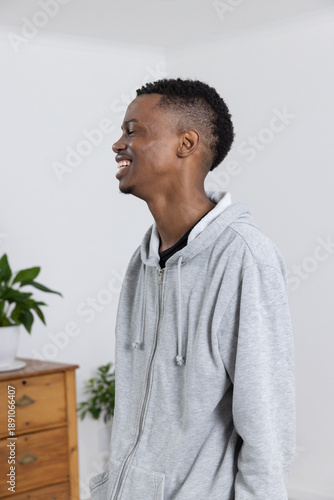 Man in zip-up hoodie standing in white corner with wooden drawers, green plants, copy space