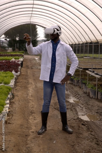 Researcher wearing VR headset is exploring hydroponic lettuce troughs inside hoop-style greenhouse