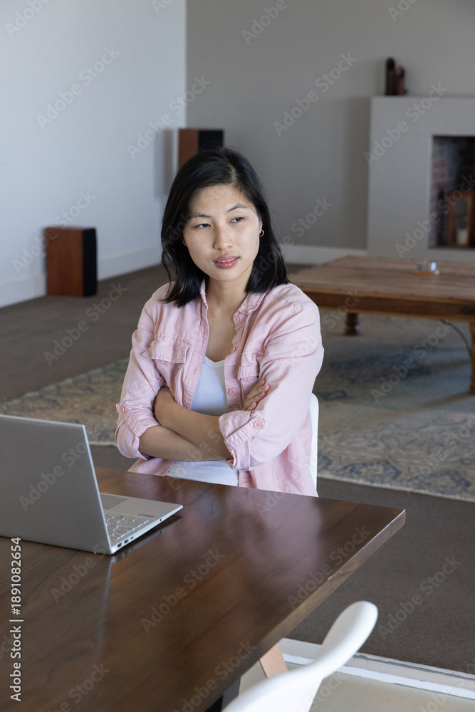Fototapeta premium Asian korean woman sitting at table typing on silver laptop in home workspace featuring rug