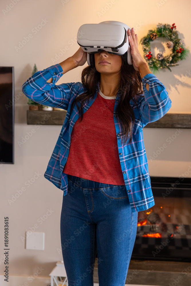 Naklejka premium Adult female adjusting vr headset before lit fireplace with holiday wreath in living room at home