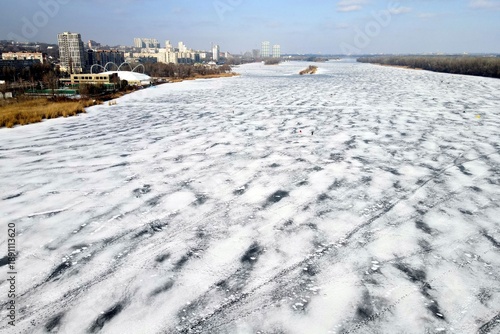 The drone flies along the icy background in winter. Beautiful blue ice frozen on the river, lake, aerial view from above.