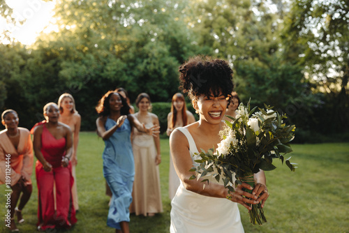 Bride tossing her bouquet surrounded by friends outdoors