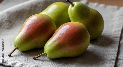 A close up view of four fresh, ripe Anjou pears displaying attractive red blush and green skin resting on fabric.