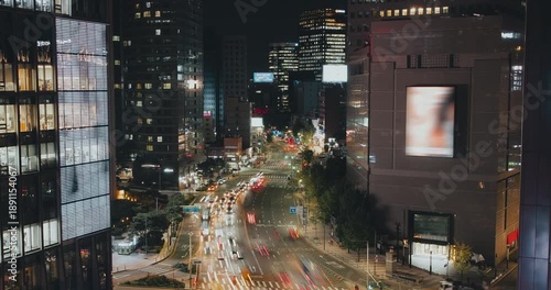 A vibrant urban night scene captures the continuous flow of traffic along a bustling city street with bright lights and towering buildings. Time-lapse, Seoul, South Korea