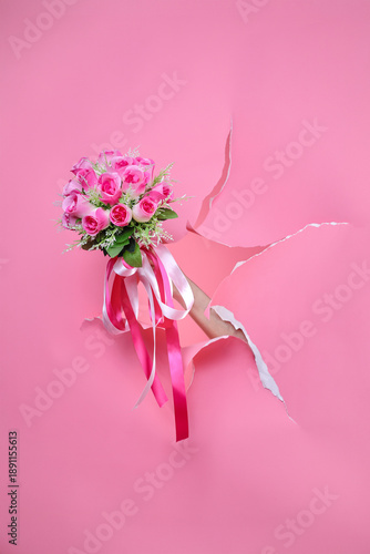 Beautiful pink flowers with long ribbons held by hand breaking through paper background for for Valentine's Day or Wedding concept.