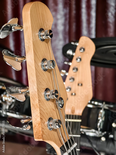 Close view of a guitar headstock with metal tuning pegs and a blurred background of drums and musical setup in a studio