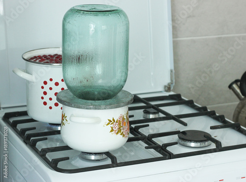 The process of sterilizing large glass jars on a gas stove in an enameled pan, preparing for rolling up cherry compote for the winter