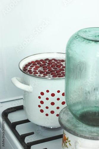 The process of sterilizing large glass jars on a gas stove in an enameled pan, preparing for rolling up cherry compote for the winter
