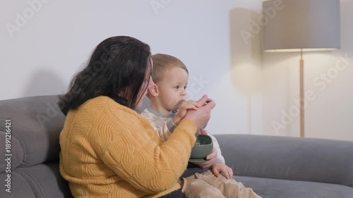 Grandmother feeding grandson with spoon on sofa