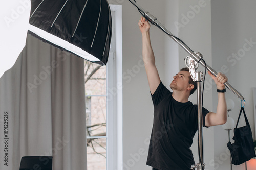 A professional photographer adjusts studio lighting equipment with a boom arm and softbox, preparing a modern indoor photoshoot setup.