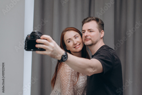 A photographer and a female model take a selfie together in a professional studio, smiling during a relaxed behind-the-scenes photoshoot moment.