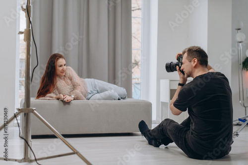 A professional photographer takes portraits of a young woman in a studio using softbox lighting, capturing a modern fashion photoshoot scene.