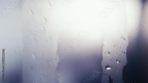 Water drops accumulating on a glass surface creating a textured background with natural light shining through, showing condensation and liquid patterns