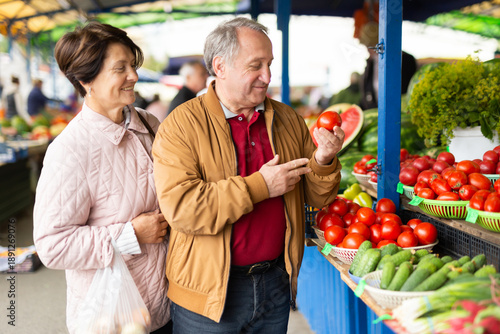 elderly man and woman buy tomatoes at an open market.