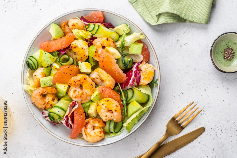 Fototapeta premium Fresh shrimp salad with colorful vegetables and dressing served in a bowl on a kitchen table