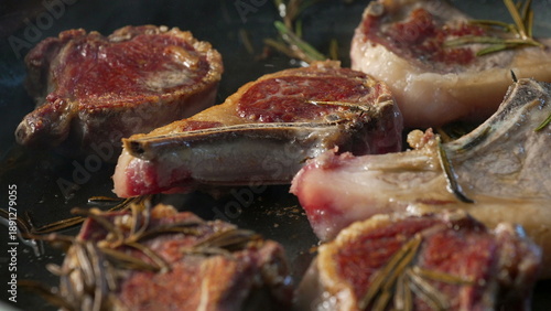 Fotografie Lamb chops browning in pan with rosemary sprigs, developing seared crust on surf