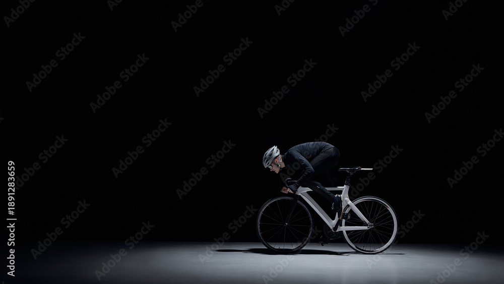 Naklejka premium Cyclist riding road bike under dramatic studio lighting. Concept of elite cycling, intense training, speed performance, professional sport, focus and discipline, dark minimal background.