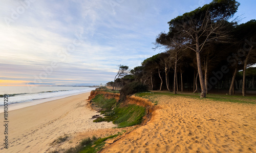 Beautiful sandy beach with red rocks and cliffs. Sunset at dusk with shallow waves on the Atlantic coast in Praia de Loule Velho, Algarve, Portugal