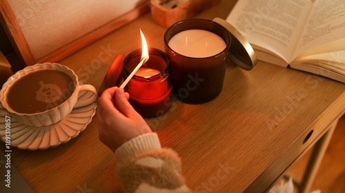 Cozy evening scene with a hand lighting a candle next to coffee and a book