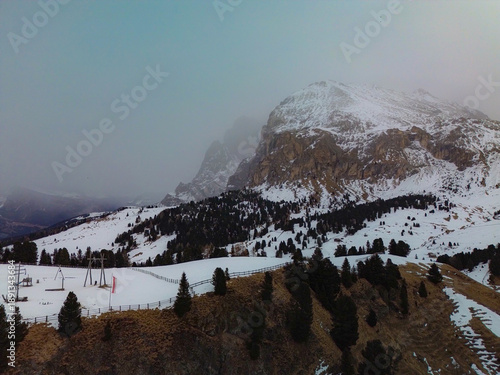 Drone view of the Alpe di Siusi (Seiser Alm) in the Italian Dolomites. Snow-capped slopes and dark coniferous forests of the South Tyrolean Alps in winter. Cinematic winter sunset in the Dolomites