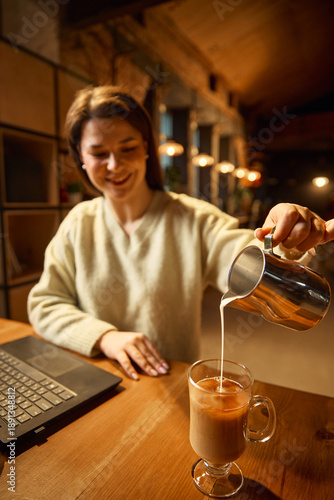 Wallpaper Mural Woman smiling while pouring milk into coffee at wooden table. Concept of customer satisfaction visuals, cafe service promotion, beverage experience marketing for hospitality brands. Torontodigital.ca
