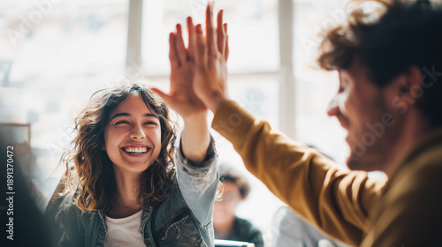 A high-quality lifestyle photo of two happy young startup employees giving a high five during a meeting, celebrating success and teamwork in a bright, modern office environment.