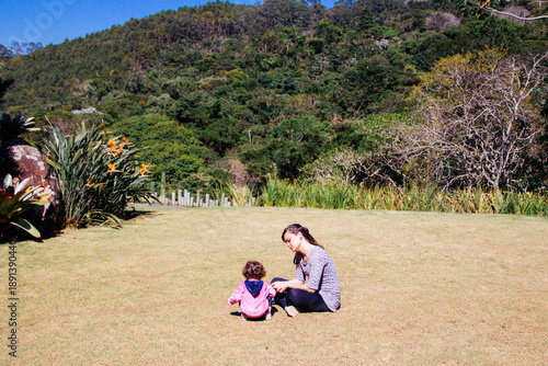 Mother and daughter sitting in a public park playing on a sunny day, Brazil