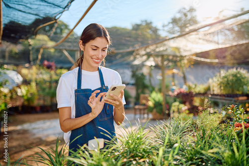 Cuadro en lienzo Young florist in a sunny garden center uses a smartphone app to manage inventory