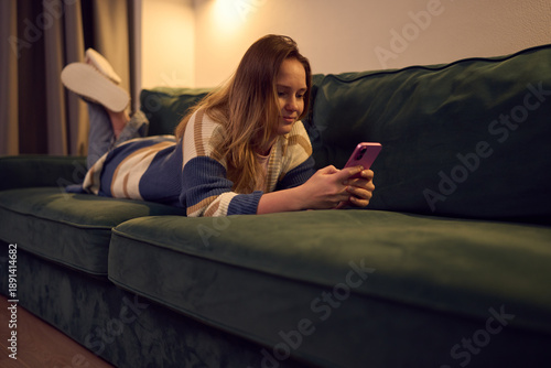 Woman lying on couch using smartphone during quiet evening